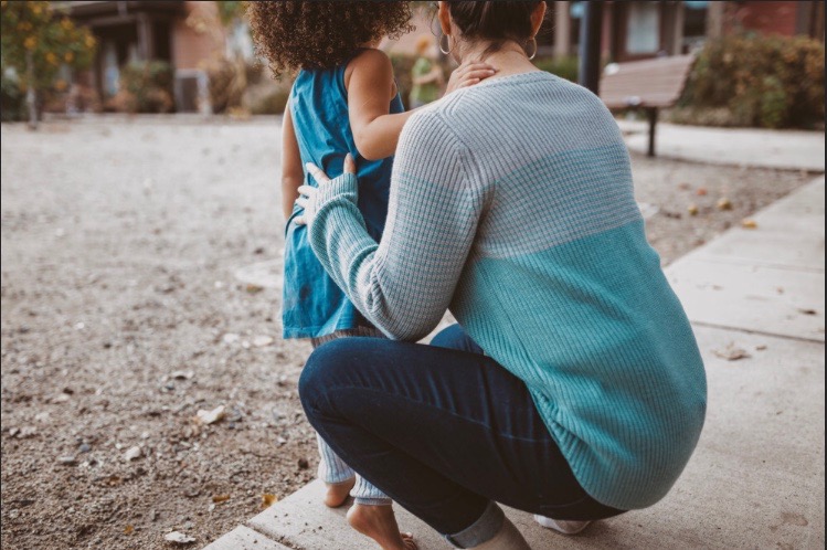 An educator kneeling down to connect with a young child outdoors